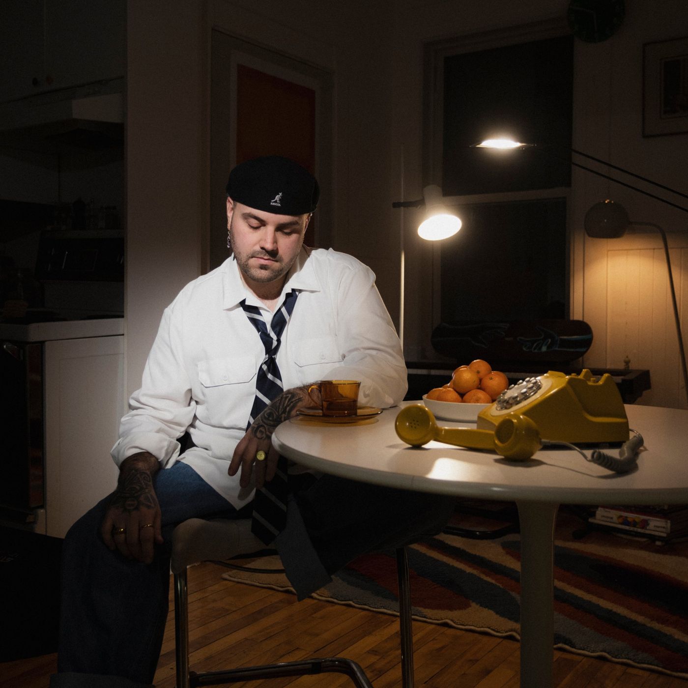 Yan Etchevary assis à une table ronde, sous une lampe, avec un téléphone jaune et un bol de mandarines