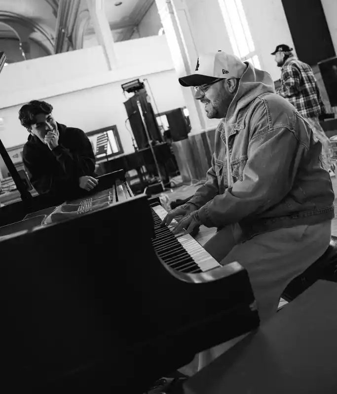 Yan joue du piano à queue, casquette sur la tête, au camp d'écriture Foyer Foyer