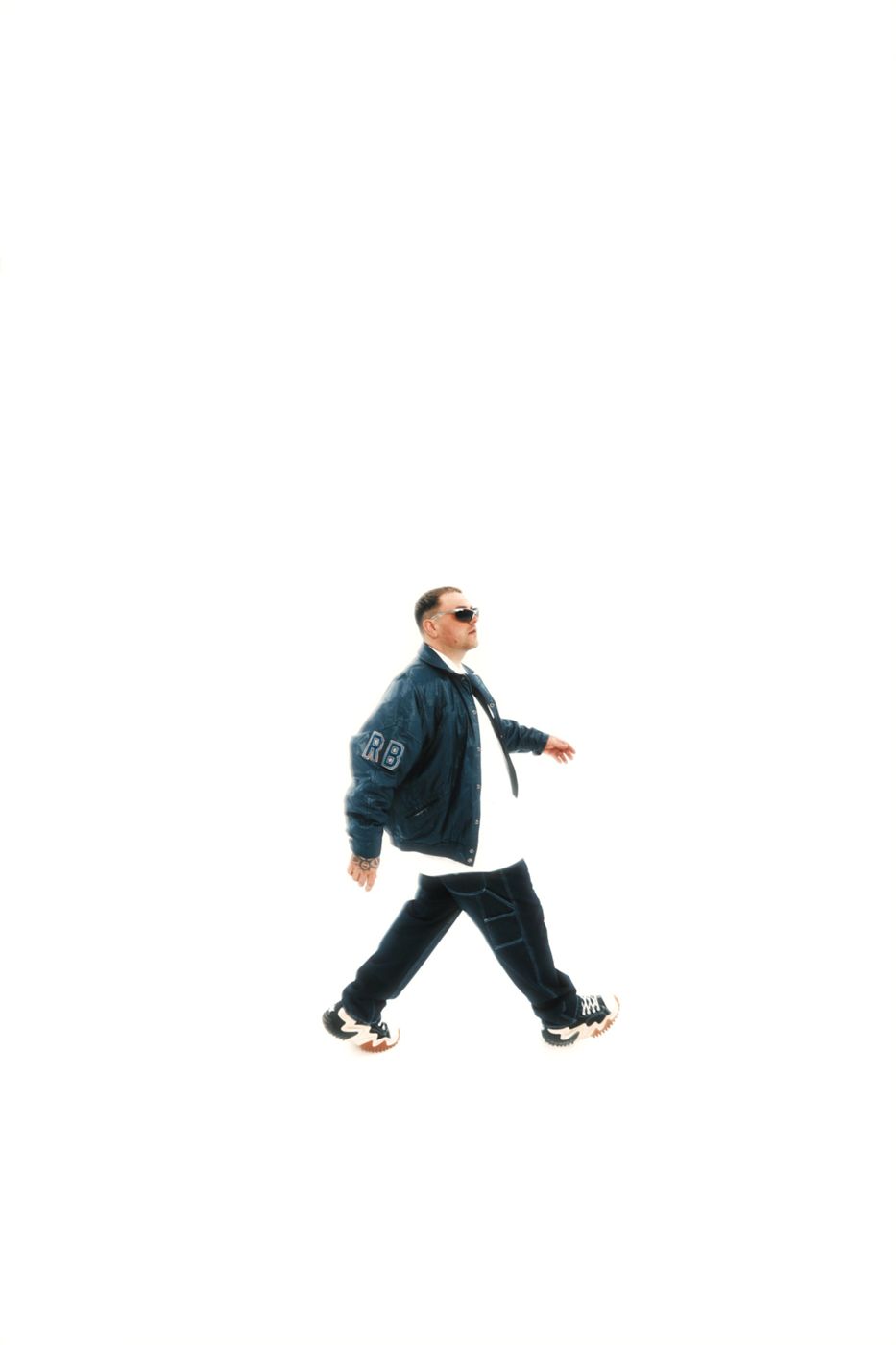 Yan marche de profil, veste bleue et lunettes, sur fond blanc